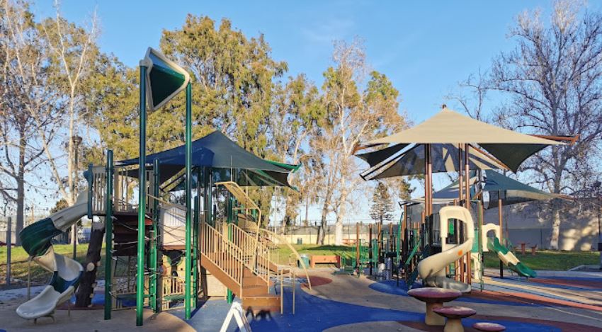 Aerial view of Parthenia Park showcasing green lawns, walking paths, and surrounding trees under a clear blue sky.