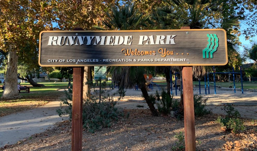 A scenic view of Runnymede Park featuring a lush green landscape, a winding path, and trees under a clear blue sky.