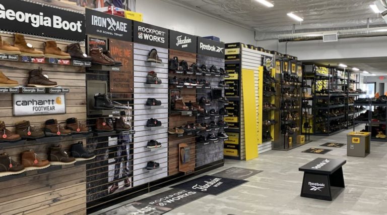 A spacious interior of a work boot warehouse showcasing various styles and sizes of work boots arranged on shelves, with bright lighting illuminating the area.