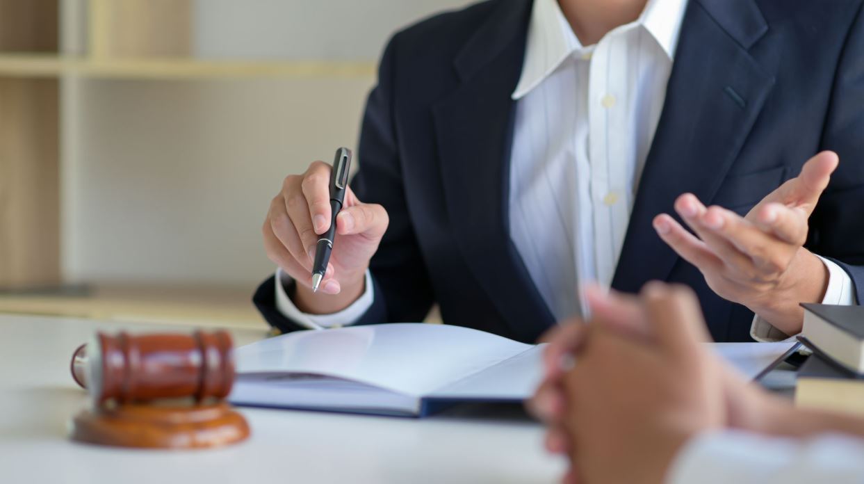 A personal injury attorney sitting at a desk with a laptop, reviewing documents, and taking notes in an office setting.